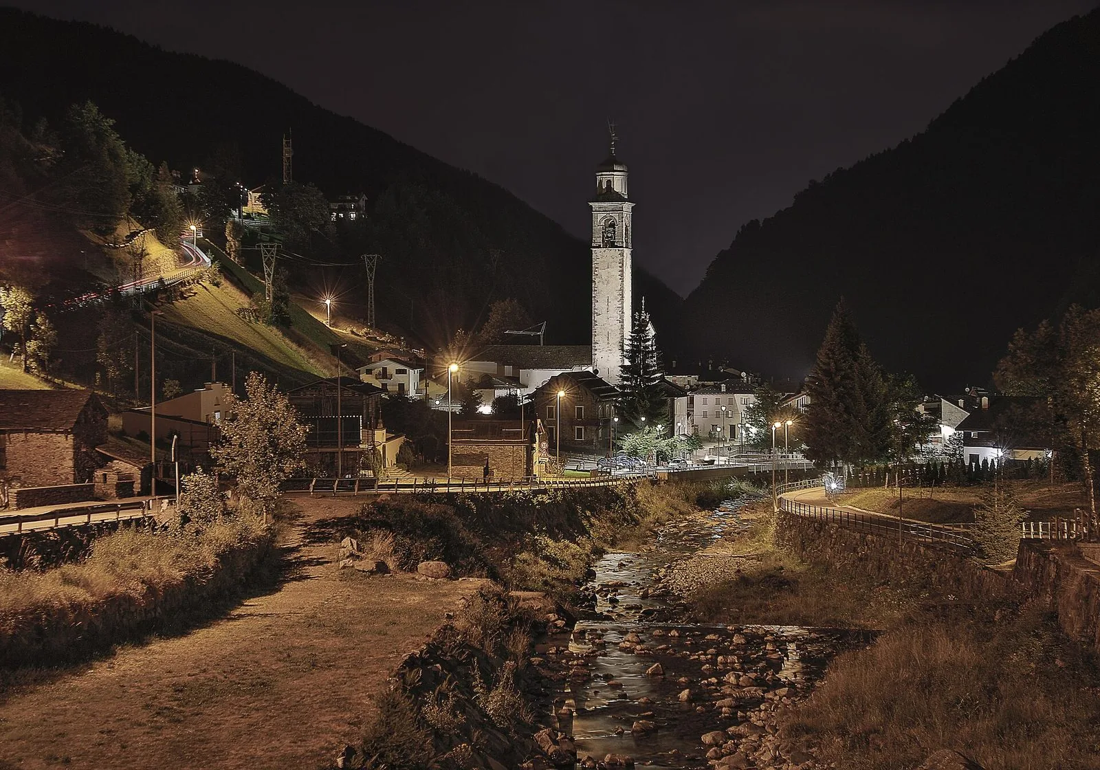 Il paese di Gerola Alta di sera, con il campanile illuminato e il torrente Bitto in primo piano