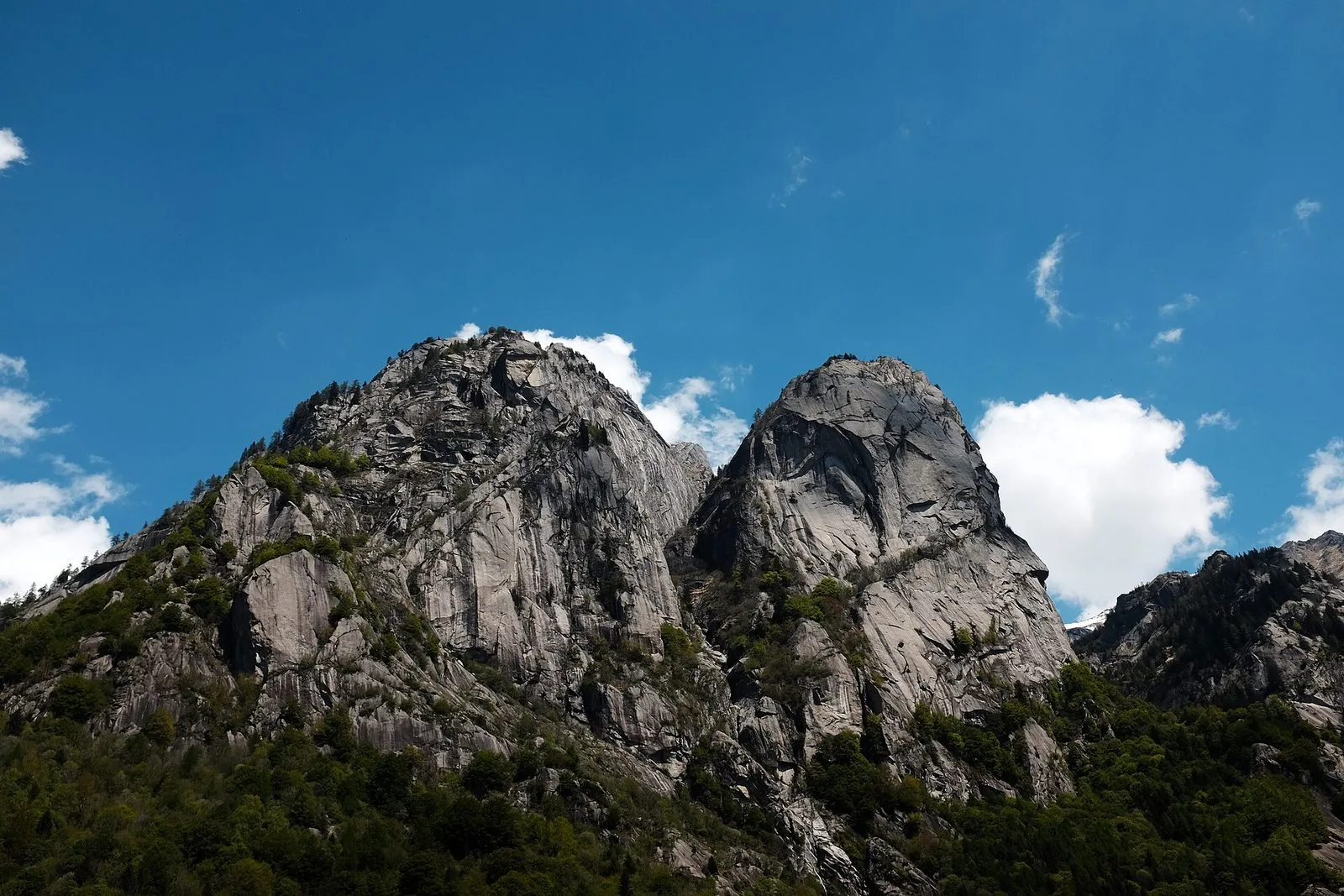 Pareti di granito della Val di Mello sopra i boschi, sotto un cielo azzurro